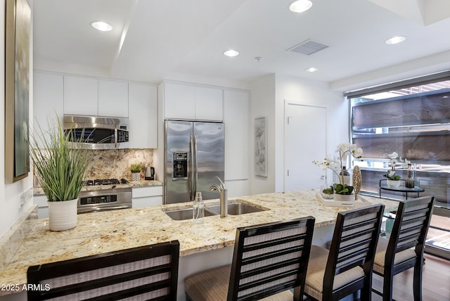 kitchen with a breakfast bar area, stainless steel appliances, tasteful backsplash, a sink, and modern cabinets