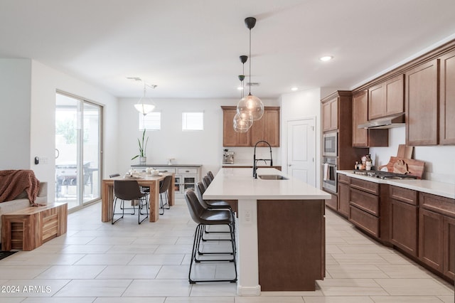 kitchen with appliances with stainless steel finishes, sink, a kitchen breakfast bar, decorative light fixtures, and a kitchen island with sink