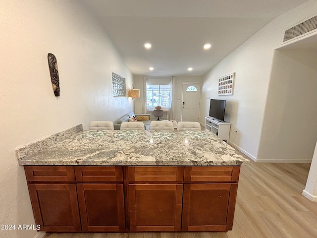 kitchen with light stone counters, light wood finished floors, lofted ceiling, visible vents, and open floor plan