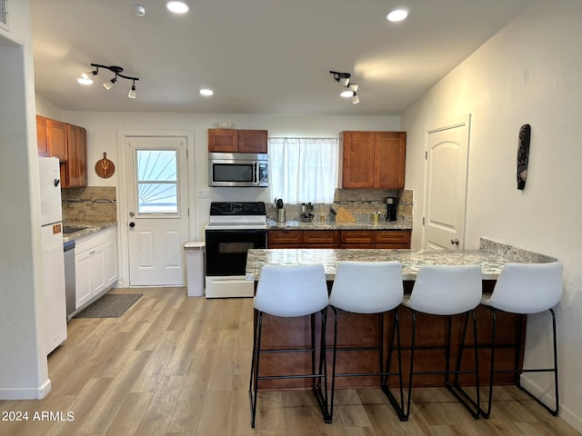 kitchen with stainless steel appliances, backsplash, light wood-style flooring, and a kitchen breakfast bar