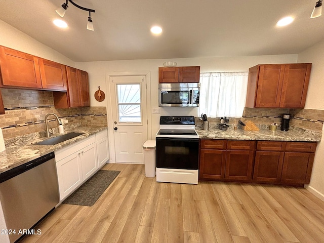 kitchen featuring brown cabinets, a sink, stainless steel appliances, light wood-style floors, and backsplash