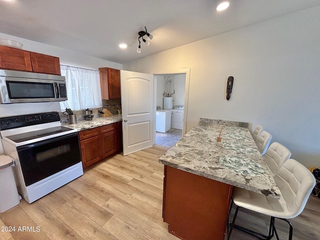 kitchen featuring light wood-style flooring, a breakfast bar, range with electric stovetop, independent washer and dryer, and stainless steel microwave