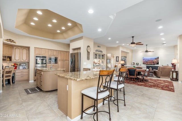 kitchen featuring a kitchen island with sink, a breakfast bar area, ceiling fan, light stone countertops, and stainless steel appliances