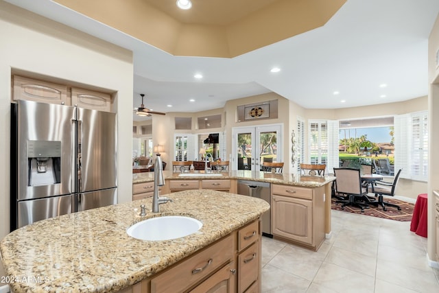 kitchen featuring light brown cabinets, a center island with sink, sink, light stone counters, and stainless steel appliances