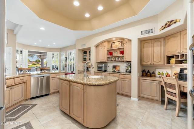 kitchen with a tray ceiling, a kitchen island with sink, dishwasher, and light brown cabinets