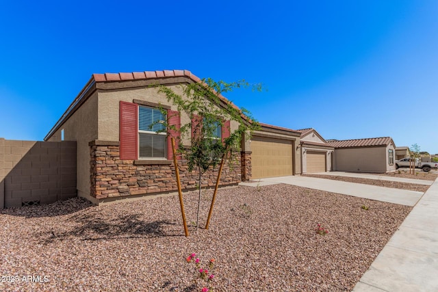 ranch-style home featuring driveway, a tile roof, stone siding, stucco siding, and an attached garage