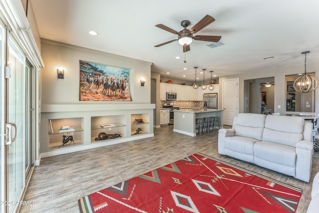 living room with ceiling fan with notable chandelier and light wood-type flooring