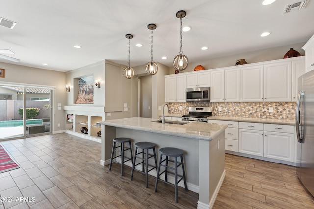 kitchen with stainless steel appliances, sink, decorative light fixtures, a center island with sink, and white cabinets