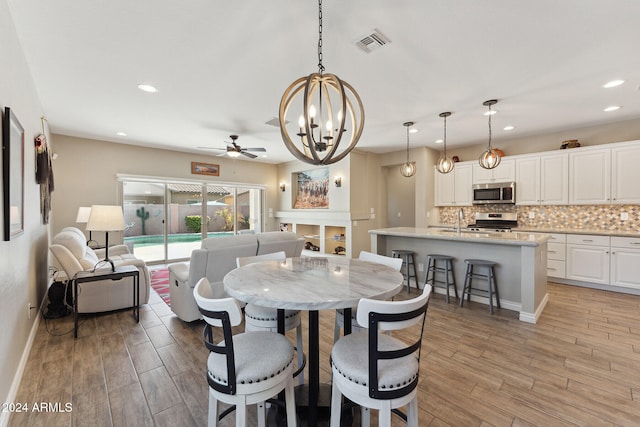 dining room with ceiling fan with notable chandelier, light hardwood / wood-style floors, and sink