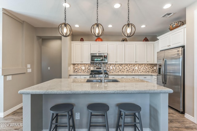 kitchen featuring light stone countertops, a center island with sink, white cabinets, and stainless steel appliances