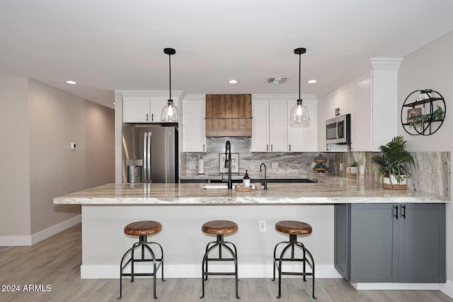 kitchen with light stone countertops, white cabinetry, kitchen peninsula, pendant lighting, and appliances with stainless steel finishes