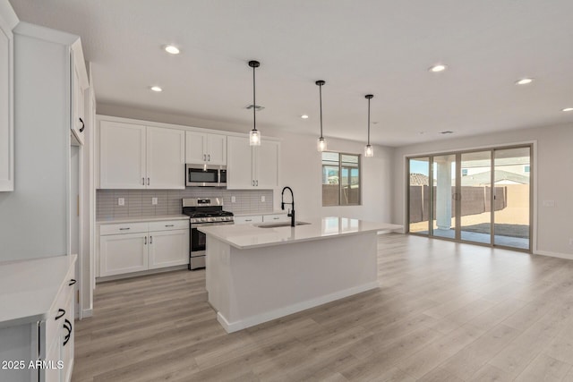 kitchen with pendant lighting, a center island with sink, sink, appliances with stainless steel finishes, and white cabinetry