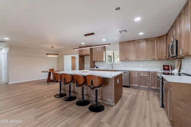 1210 W La Jolla Dr, Tempe, AZ 85282 - kitchen with stainless steel appliances, light wood-style flooring, a kitchen island, a kitchen bar, and recessed lighting