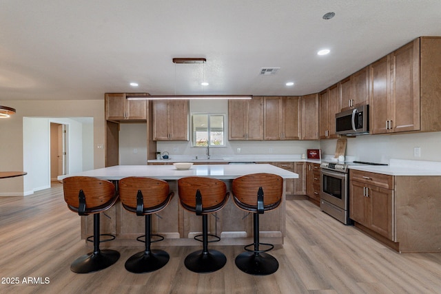 1210 W La Jolla Dr, Tempe, AZ 85282 - kitchen with appliances with stainless steel finishes, light wood finished floors, a center island, light countertops, and brown cabinetry