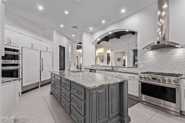 kitchen featuring visible vents, a sink, white cabinetry, wall chimney range hood, and high end appliances