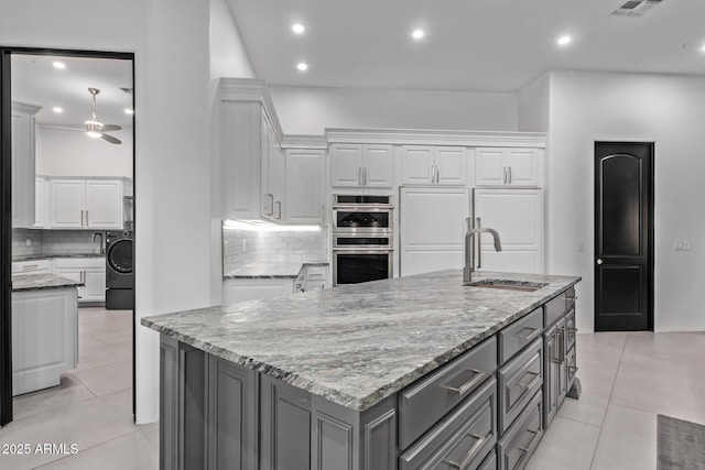 kitchen with gray cabinetry, a sink, double oven, white cabinets, and light tile patterned floors