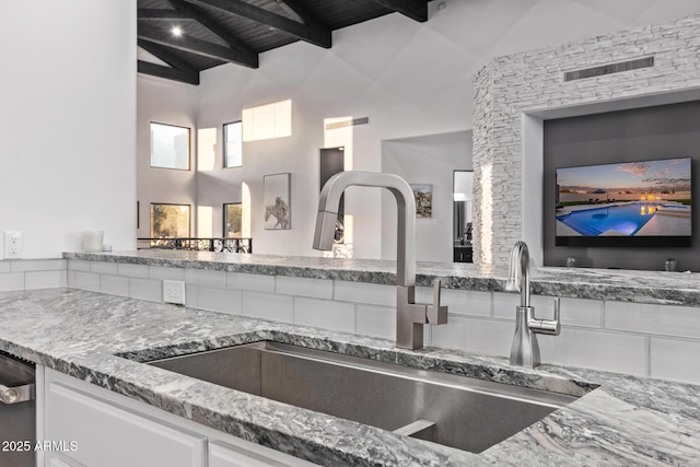 kitchen featuring visible vents, beam ceiling, stone countertops, white cabinetry, and a sink