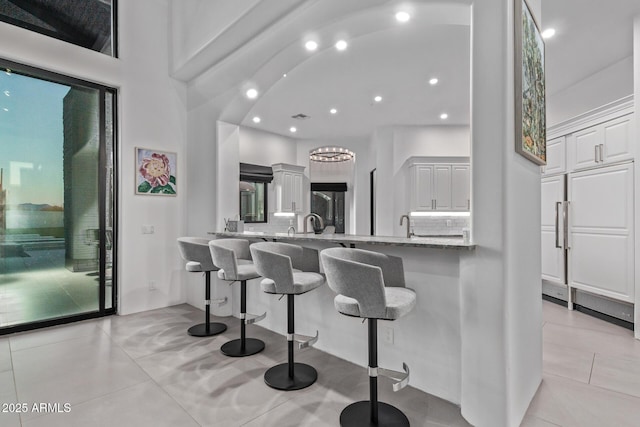 kitchen featuring light stone counters, a breakfast bar, a peninsula, white cabinetry, and tasteful backsplash