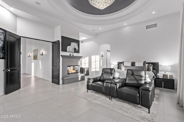 bedroom featuring a raised ceiling, a high ceiling, visible vents, and a multi sided fireplace