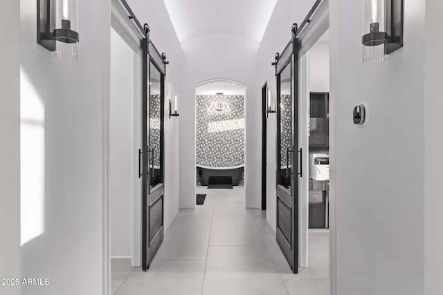 hallway featuring a barn door, light tile patterned flooring, and vaulted ceiling