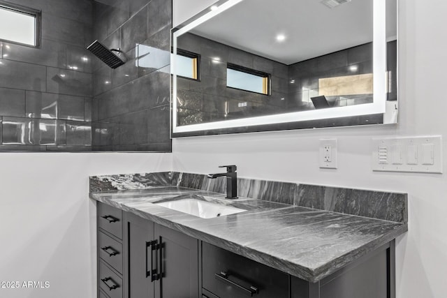 bathroom with visible vents, vanity, and a tile shower