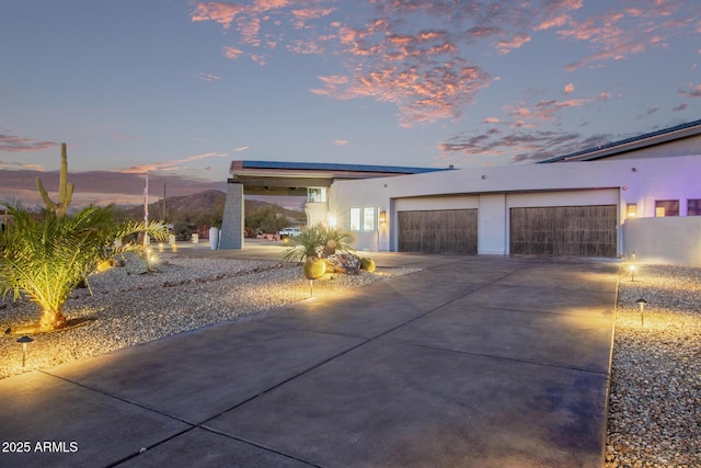 view of front of house with stucco siding, driveway, an attached garage, and solar panels