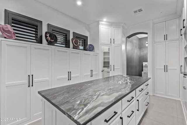 kitchen with visible vents, white cabinetry, dark stone counters, arched walkways, and light tile patterned floors