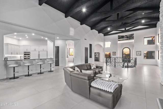 living room featuring beam ceiling, wooden ceiling, light tile patterned flooring, arched walkways, and high vaulted ceiling