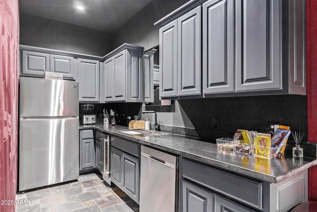 kitchen with dark countertops, stone finish flooring, gray cabinets, appliances with stainless steel finishes, and a sink