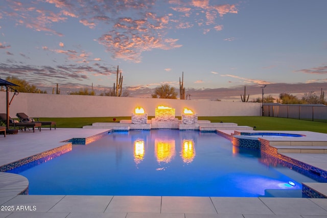 pool at dusk with a pool with connected hot tub, a fenced backyard, and a patio area