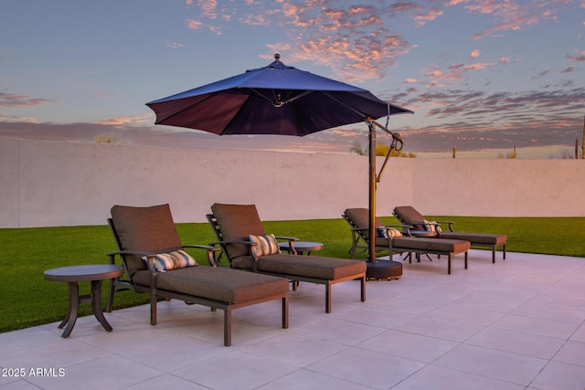 patio terrace at dusk featuring a yard and fence