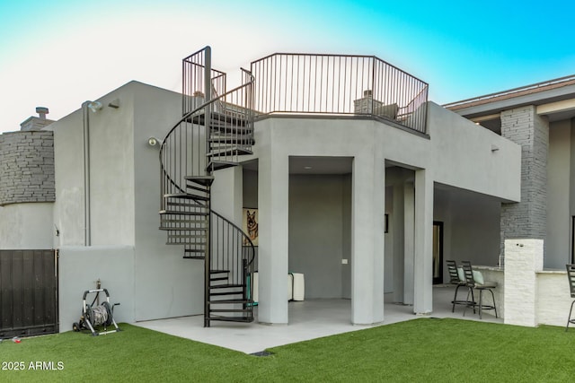 rear view of house with stucco siding, a lawn, a patio, stairway, and a balcony