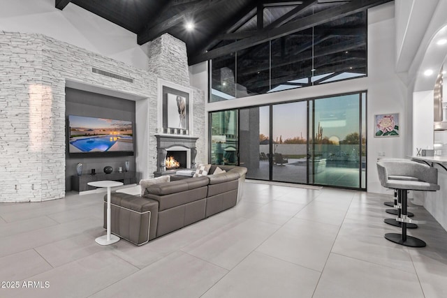 living room featuring tile patterned flooring, beamed ceiling, a warm lit fireplace, and high vaulted ceiling