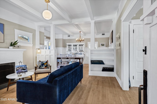 living room with a chandelier, a fireplace, beamed ceiling, and light wood finished floors