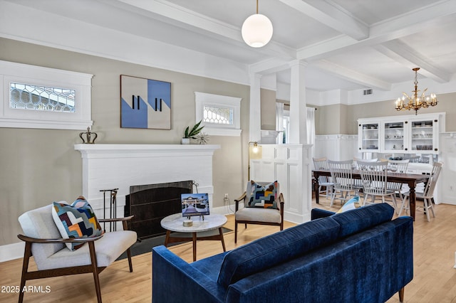 living area featuring light wood-style flooring, plenty of natural light, beam ceiling, and a brick fireplace