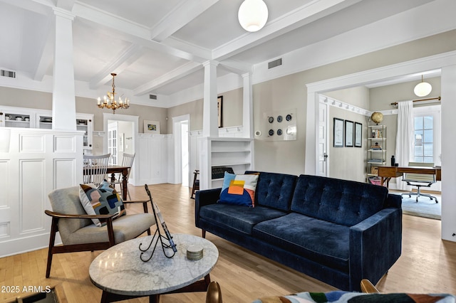 living area with light wood-style floors, a fireplace, beam ceiling, and ornate columns