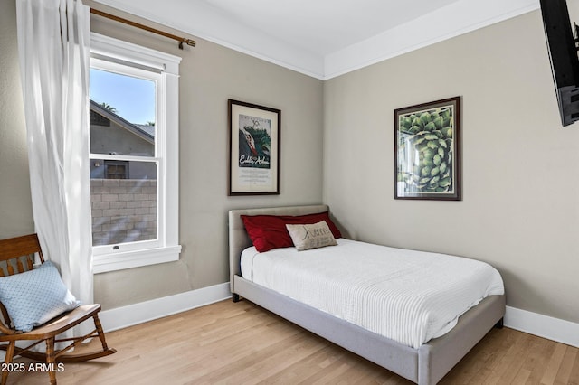 bedroom featuring ornamental molding, light wood finished floors, and baseboards