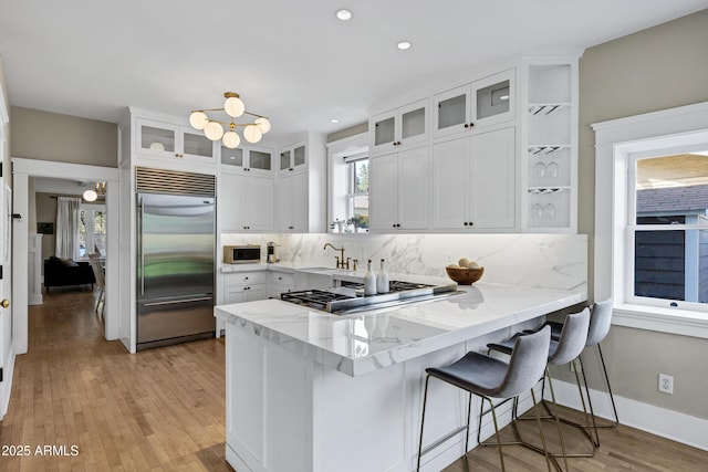 kitchen with decorative backsplash, a peninsula, light stone countertops, stainless steel appliances, and white cabinetry