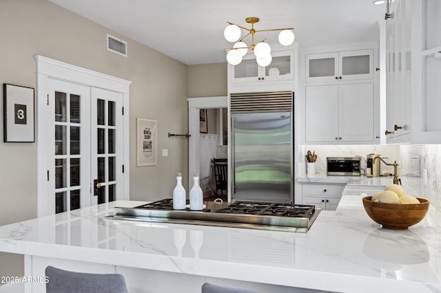 kitchen with white cabinetry, visible vents, appliances with stainless steel finishes, tasteful backsplash, and glass insert cabinets