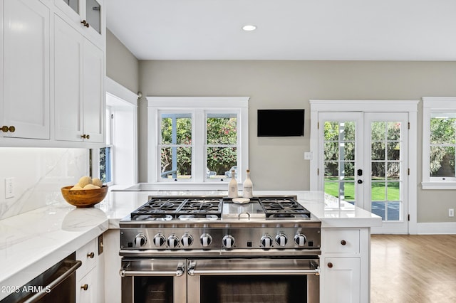 kitchen with light stone counters, light wood-type flooring, double oven range, and white cabinetry