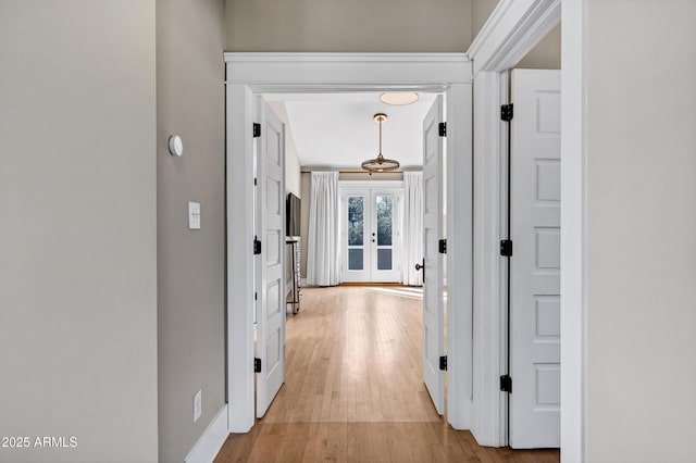 hallway with baseboards, french doors, and light wood-style floors