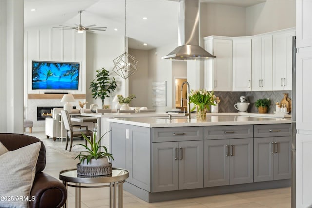 kitchen featuring open floor plan, light countertops, wall chimney range hood, and gray cabinetry