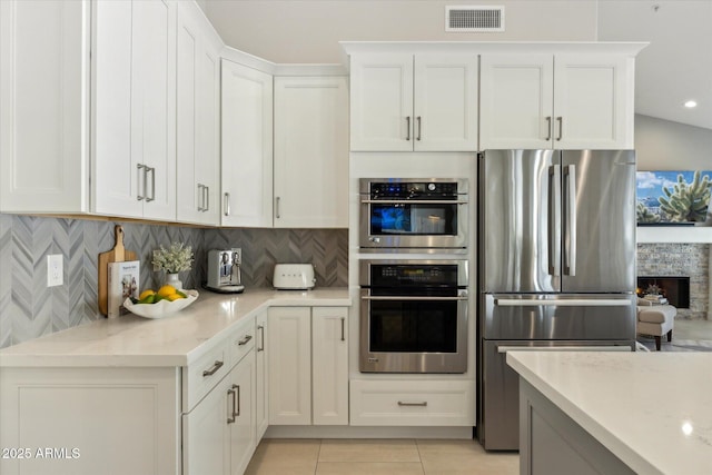 kitchen featuring visible vents, decorative backsplash, appliances with stainless steel finishes, white cabinetry, and light tile patterned flooring