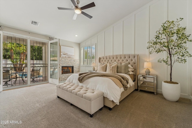 carpeted bedroom with a fireplace, visible vents, a decorative wall, ceiling fan, and access to outside