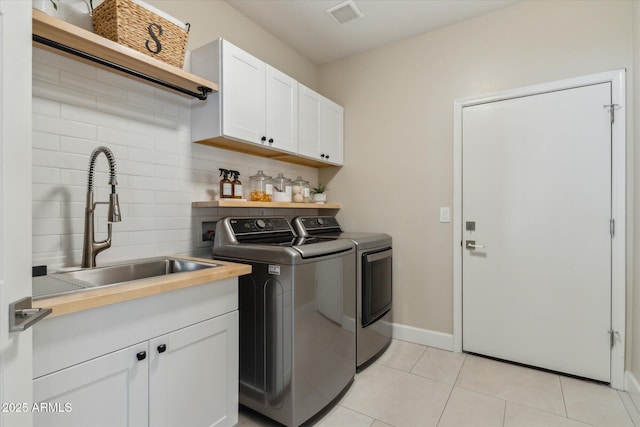 clothes washing area with light tile patterned floors, a sink, visible vents, washer and dryer, and cabinet space