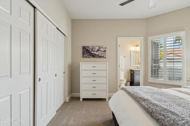 bedroom with a closet, light carpet, connected bathroom, ceiling fan, and baseboards