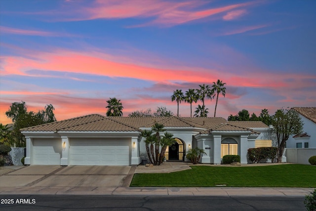 mediterranean / spanish-style home with concrete driveway, a lawn, an attached garage, fence, and stucco siding