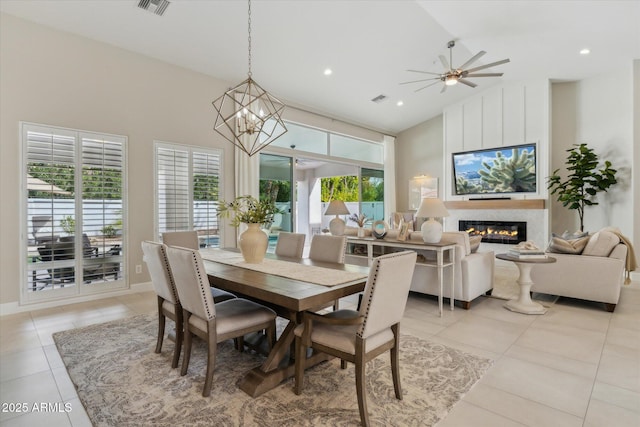 dining room featuring light tile patterned floors, high vaulted ceiling, ceiling fan with notable chandelier, and a fireplace