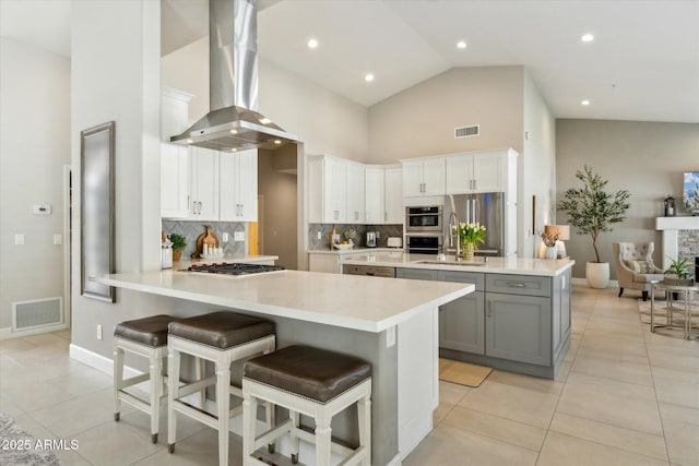 kitchen with a peninsula, island exhaust hood, visible vents, and gray cabinetry