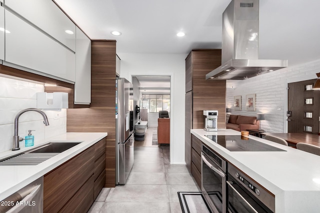 kitchen featuring modern cabinets, island exhaust hood, stainless steel appliances, light countertops, and a sink